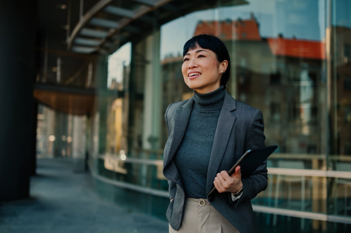 Businesswoman is smiling while walking outside her office building, holding a tablet