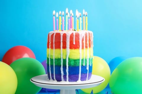 Delicious rainbow birthday cake with burning candles and balloons