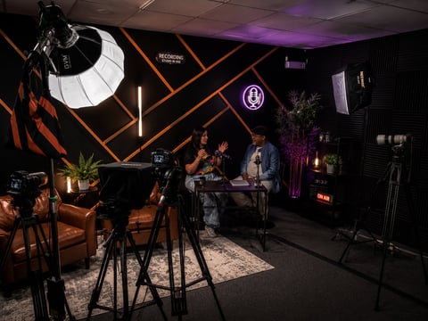 Professional studio set with neon orange geometric backdrop, film cameras, and interview setup with purple lighting