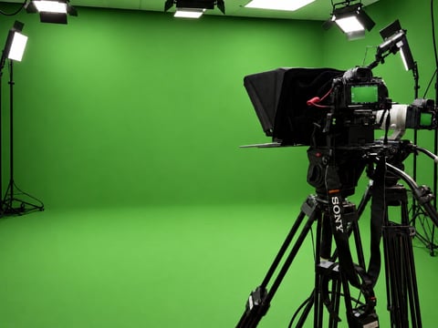 Professional video camera on tripod in bright green screen studio with LED lighting fixtures mounted on walls and ceiling