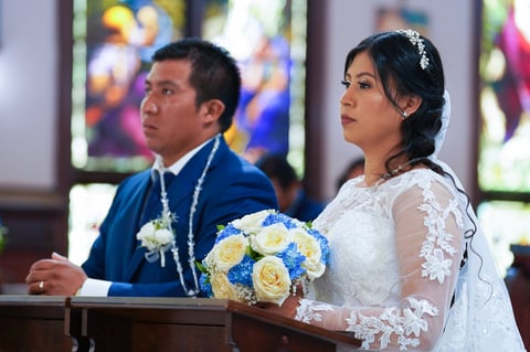 Bride and groom at wedding ceremony with blue and white bouquet, church interior with stained glass windows in background