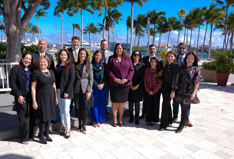 Group of professionals standing together outdoors on a sunny day with palm trees and blue sky in the background