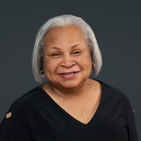 Portrait of a smiling woman with short white hair wearing a black v-neck shirt against a dark gray background