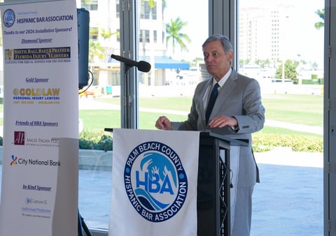 Man in suit speaking at podium with LBA logo at a business event with sponsor logos visible