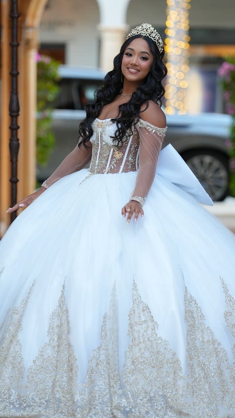 Young woman in an elegant white ball gown with beaded details, tiara, and long dark hair poses for a formal portrait outdoors