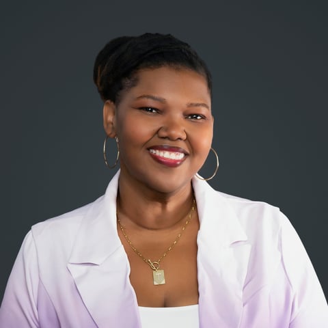 Professional headshot of a woman wearing a light purple blazer and hoop earrings, smiling against a dark gray background
