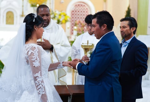 Bride in white lace dress exchanges rings with groom in blue suit during wedding ceremony in church