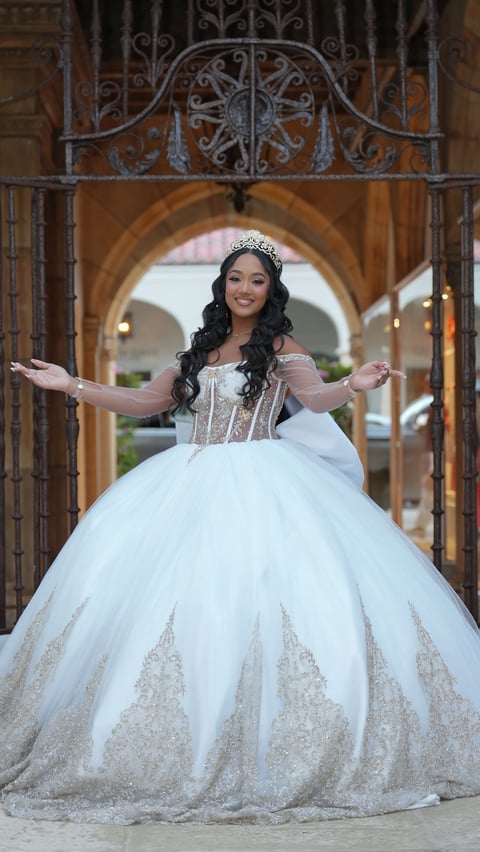 Woman in an ornate white ball gown with tiara and long dark wavy hair, arms outstretched under an elaborate wrought iron archway