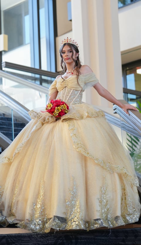 Woman in champagne ball gown with tiara holding red rose bouquet on modern staircase