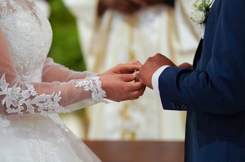 Bride in white lace dress and groom in navy suit exchanging rings during wedding ceremony