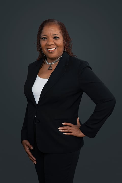 Professional portrait of a smiling woman wearing a black blazer and white top against a gray background