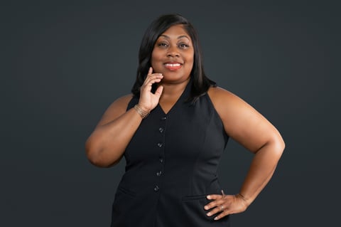 Woman in black sleeveless shirt smiling with hand to face against gray background