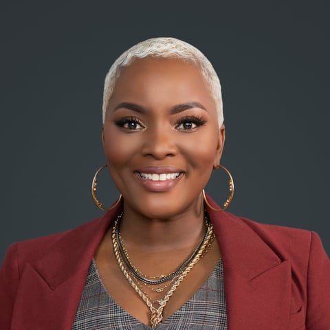 Portrait of a smiling woman with short white hair, hoop earrings, and a burgundy blazer against a dark background