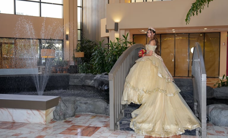 Bride in yellow ball gown posing at staircase in modern hotel lobby with fountain and plants