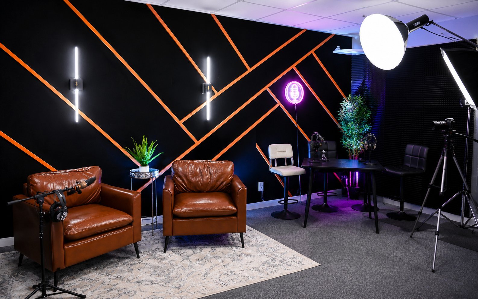 Modern studio with two brown leather armchairs, orange neon geometric wall patterns, and professional lighting equipment on dark background