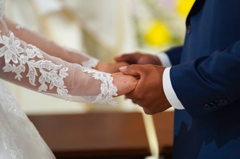 Bride and groom holding hands during wedding ceremony, bride wearing white lace dress