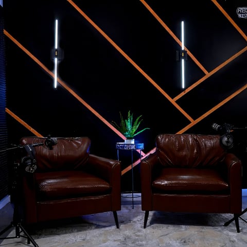 Two burgundy leather armchairs facing each other with a small table between them under geometric neon orange and white ceiling design