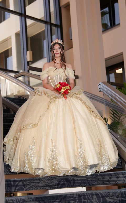 Woman in cream-colored ball gown with tiara and red bouquet standing on modern building stairs