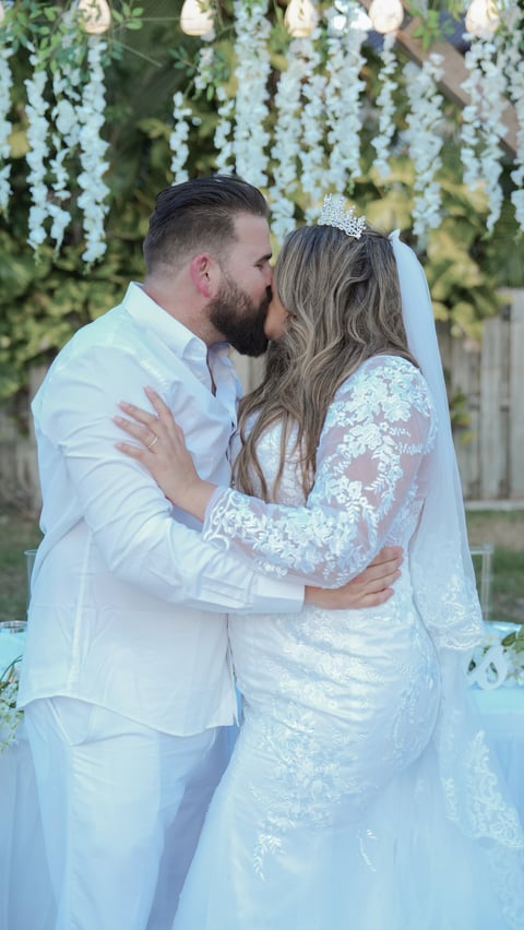 Bride and groom kissing at outdoor wedding ceremony under floral archway with hanging white flowers