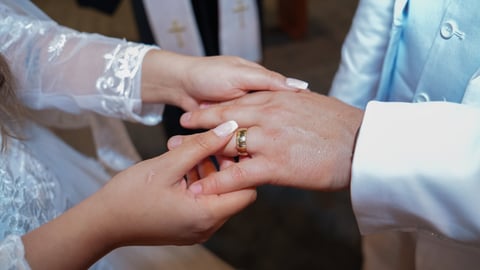 Bride and groom exchanging wedding rings during ceremony, close-up of their hands showing wedding bands