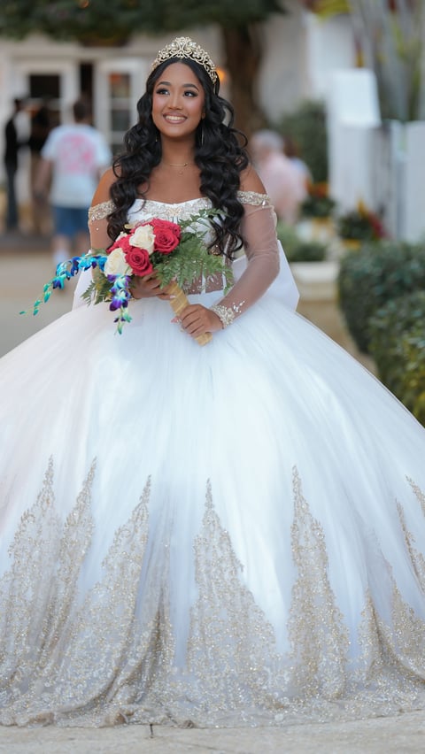 Bride in elegant white ball gown with tiara holding colorful bouquet, posing outdoors at wedding venue