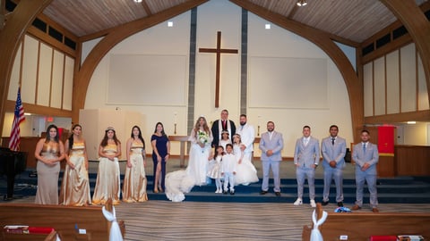 Wedding party poses together on church altar with bride, groom, and wedding guests in formal attire