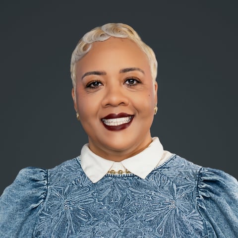 Smiling woman with short white hair wearing a blue patterned top with white collar against gray background